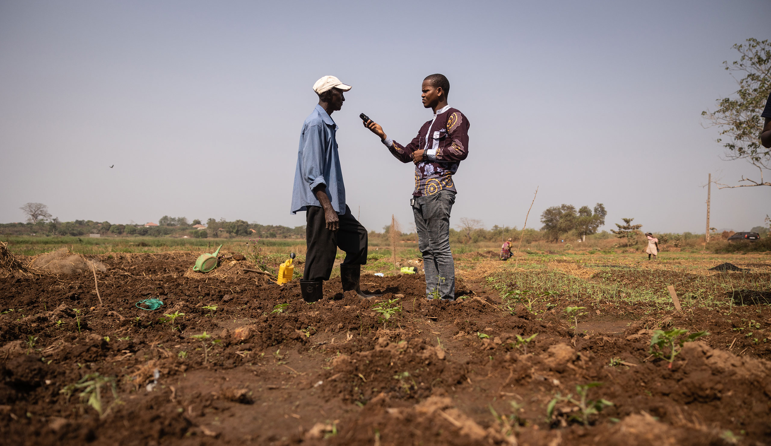Alpha Oumar Bagou Barry, journalist with the Association of Scientific Journalists of Guinea (AJSG), interviews a man in the context of a micro sidewalk, in the vegetable garden of the Dogbéré district in the city of Dubréka, on February 4, 2022. © Olympia de Maismont / Fondation Hirondelle
